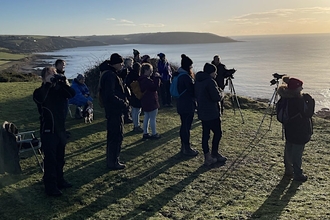 A group of people on a calm morning looking out to sea with telescopes.